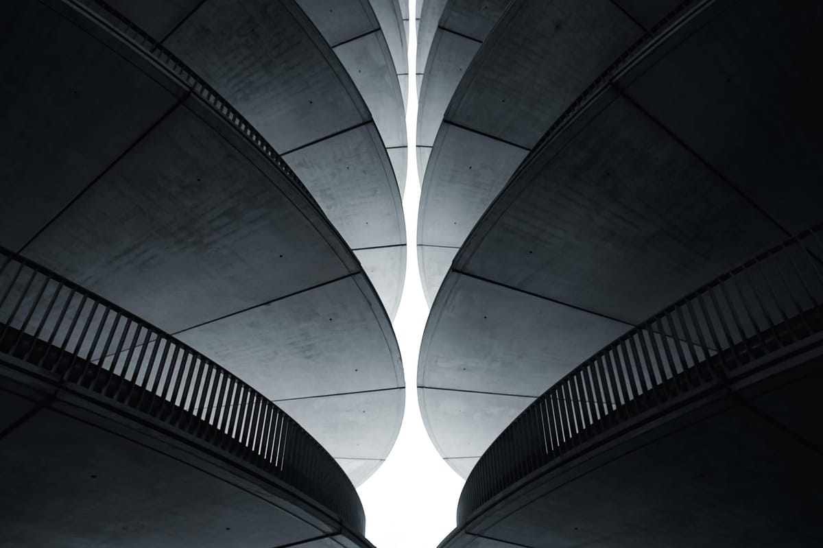 Two curved concrete structures rising symmetrically toward a narrow gap of bright sky between them.