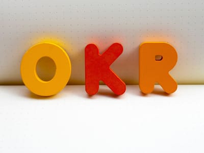 Wooden letters spelling OKR standing upright on a dot-grid notebook page.