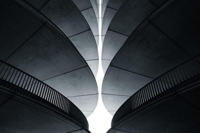 Two curved concrete structures rising symmetrically toward a narrow gap of bright sky between them.