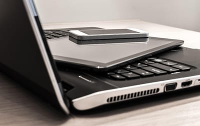 A smartphone and a tablet stacked on the keyboard of an open laptop.
